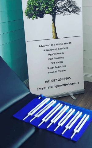 A set of tuning forks laid out beside the Whitebeam pull-up banner listing services: hypnotherapy, quit smoking, sugar reduction, fears and phobias